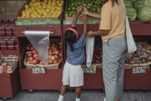 Ethnic woman choosing fruits with daughter in market, teaching honor to children